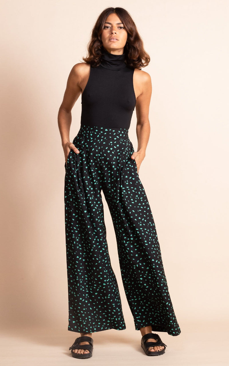 Dancing Leopard model standing with hands in trouser pockets wearing wide leg black and green dotty wide leg trousers with black bodysuit and black sandals