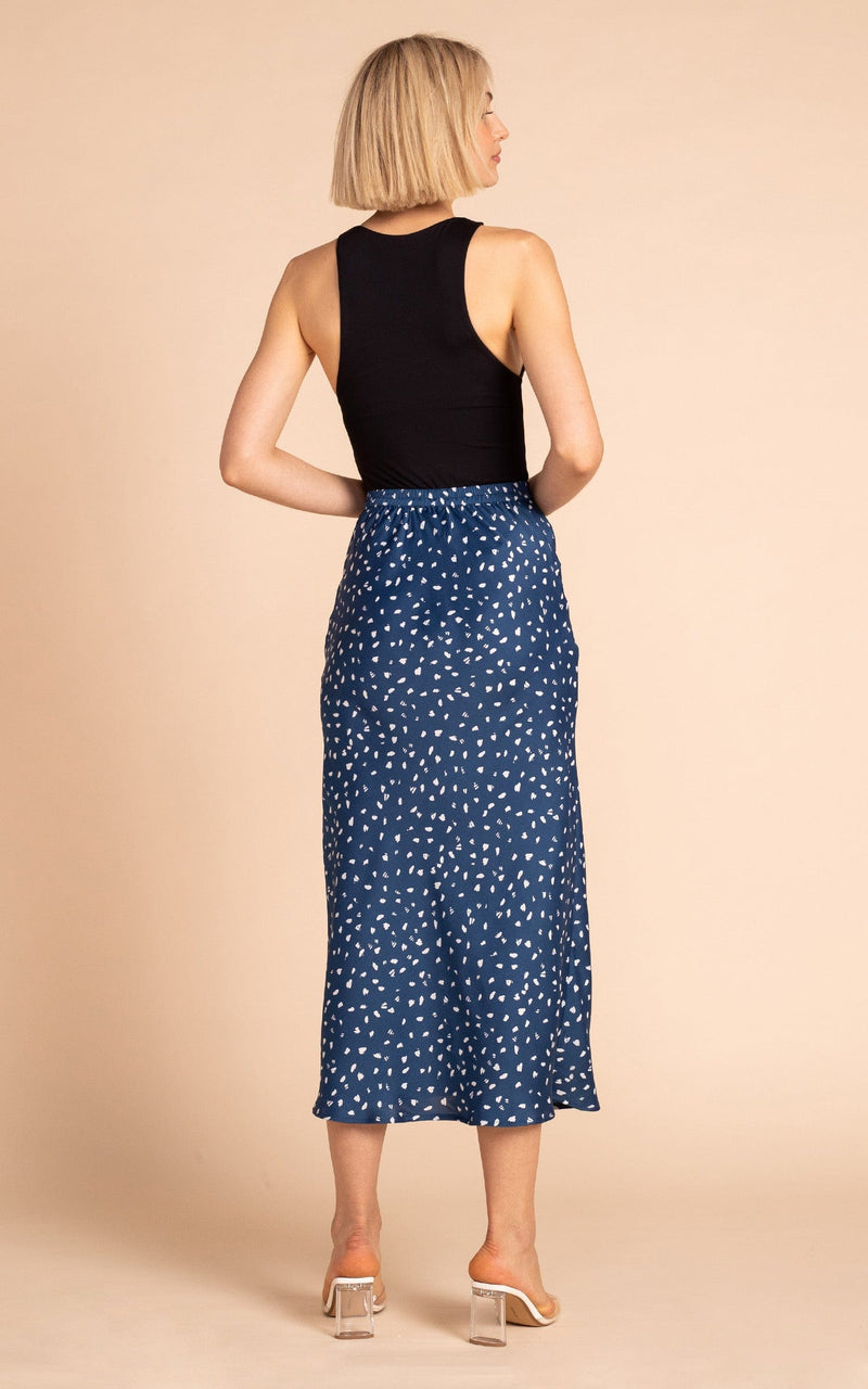 Dancing Leopard model standing backwards wearing Renzo satin midi slip skirt in abstract white on navy with black tank top and clear heels