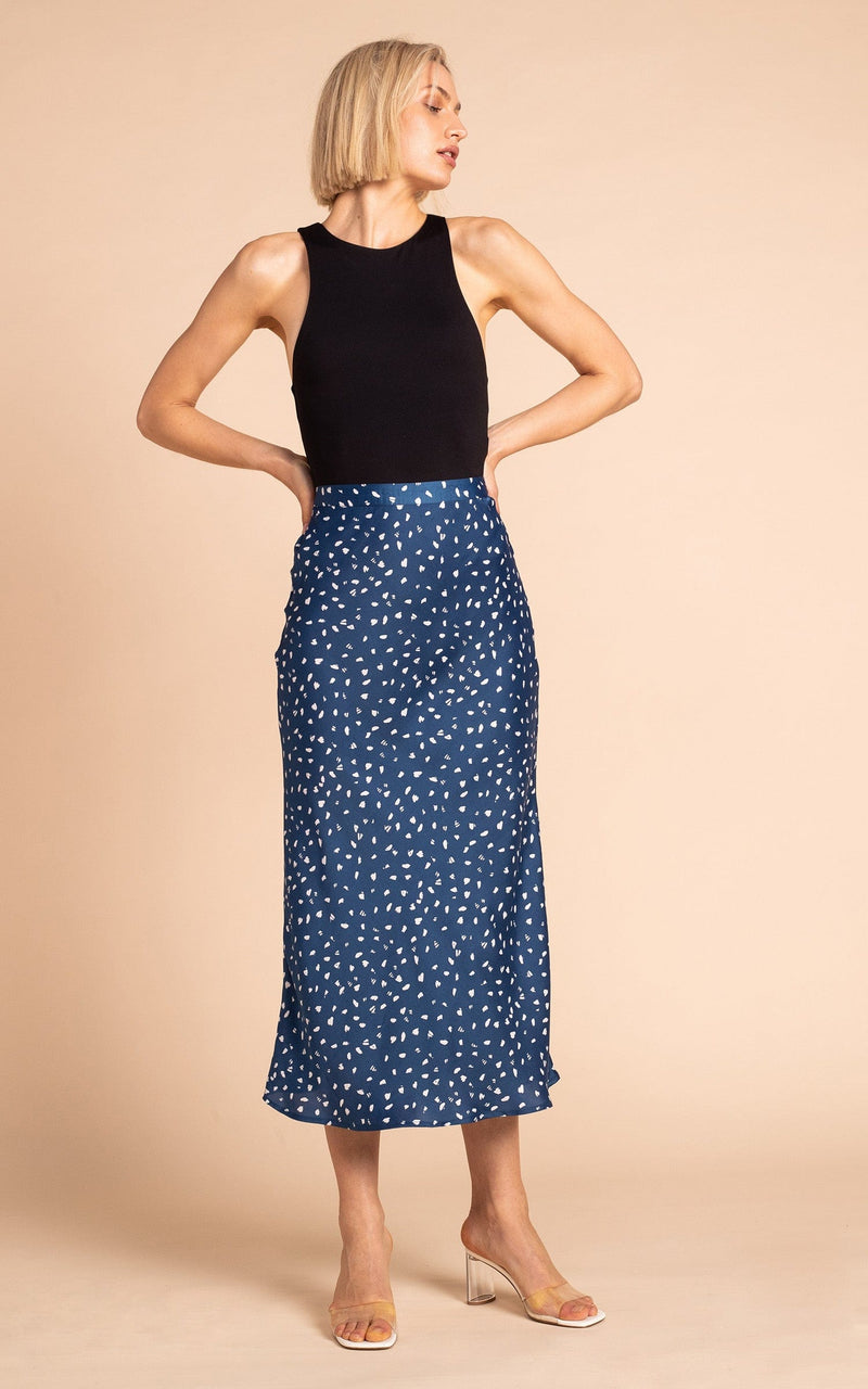 Dancing Leopard model standing wearing Renzo satin midi slip skirt in abstract white on navy with black tank top and clear heels