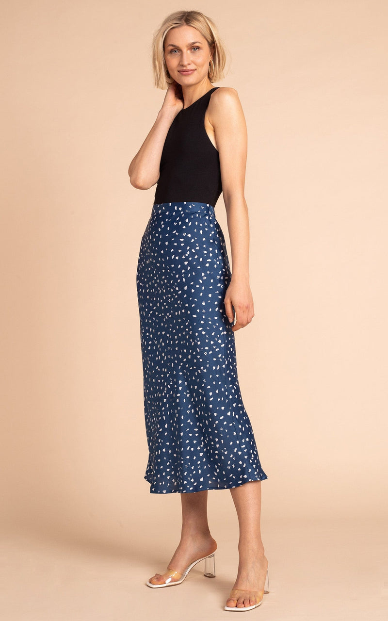 Dancing Leopard model standing wearing Renzo satin midi slip skirt in abstract white on navy with black tank top and clear heels
