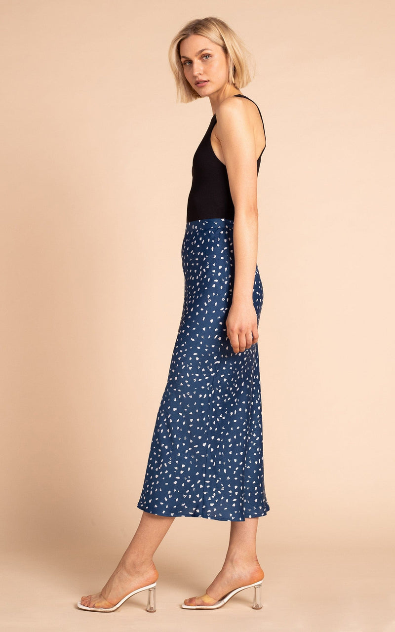 Dancing Leopard model standing sideways wearing Renzo satin midi slip skirt in abstract white on navy with black tank top and clear heels