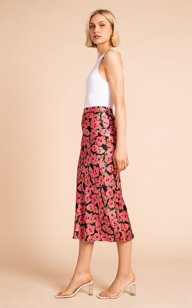 Dancing Leopard model standing sideways wearing Renzo skirt in pink on black hibiscus with white tank top and clear sandals 
