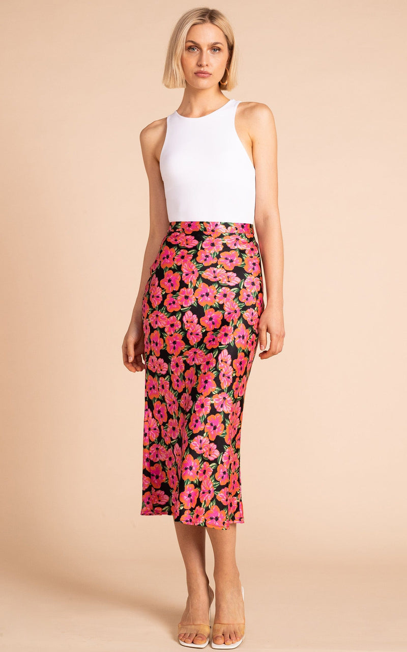 Dancing Leopard model standing wearing Renzo skirt in pink on black hibiscus with white tank top and clear sandals 
