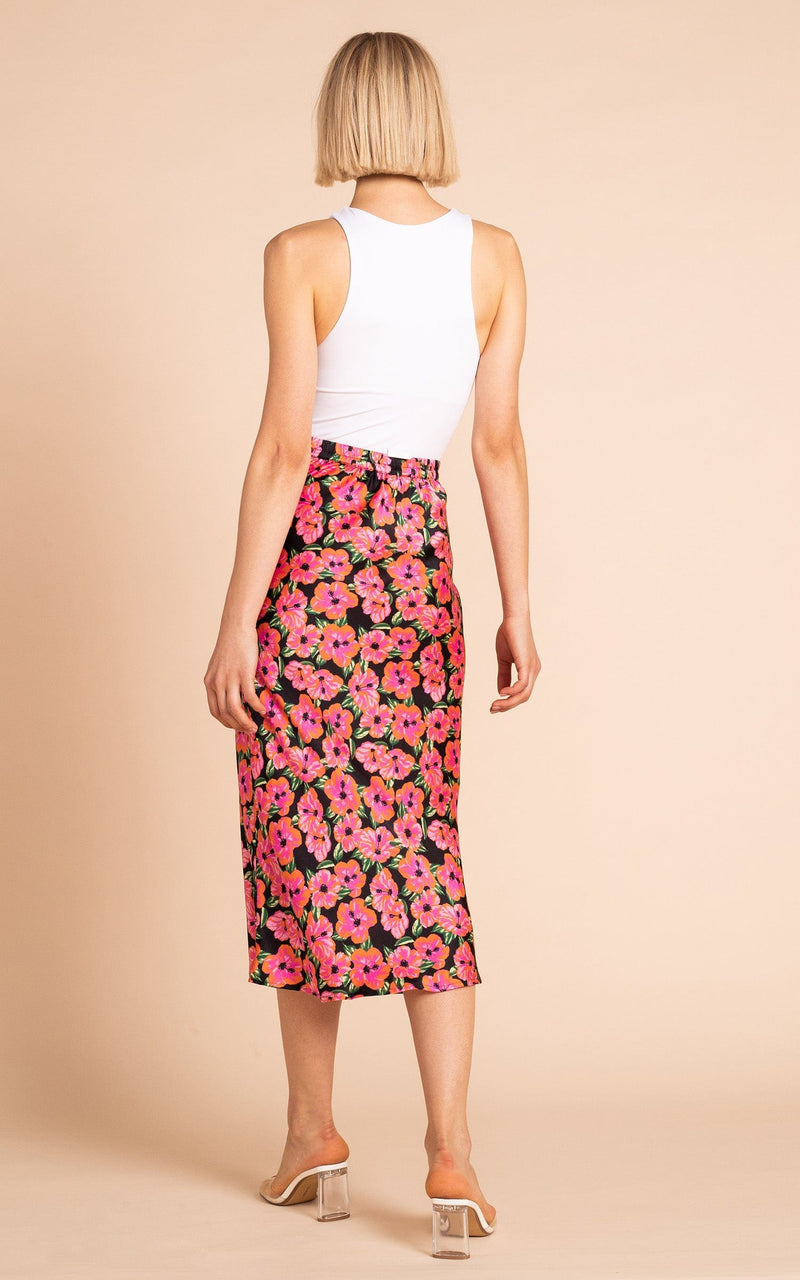 Dancing Leopard model standing backwards wearing Renzo skirt in pink on black hibiscus with white tank top and clear sandals 