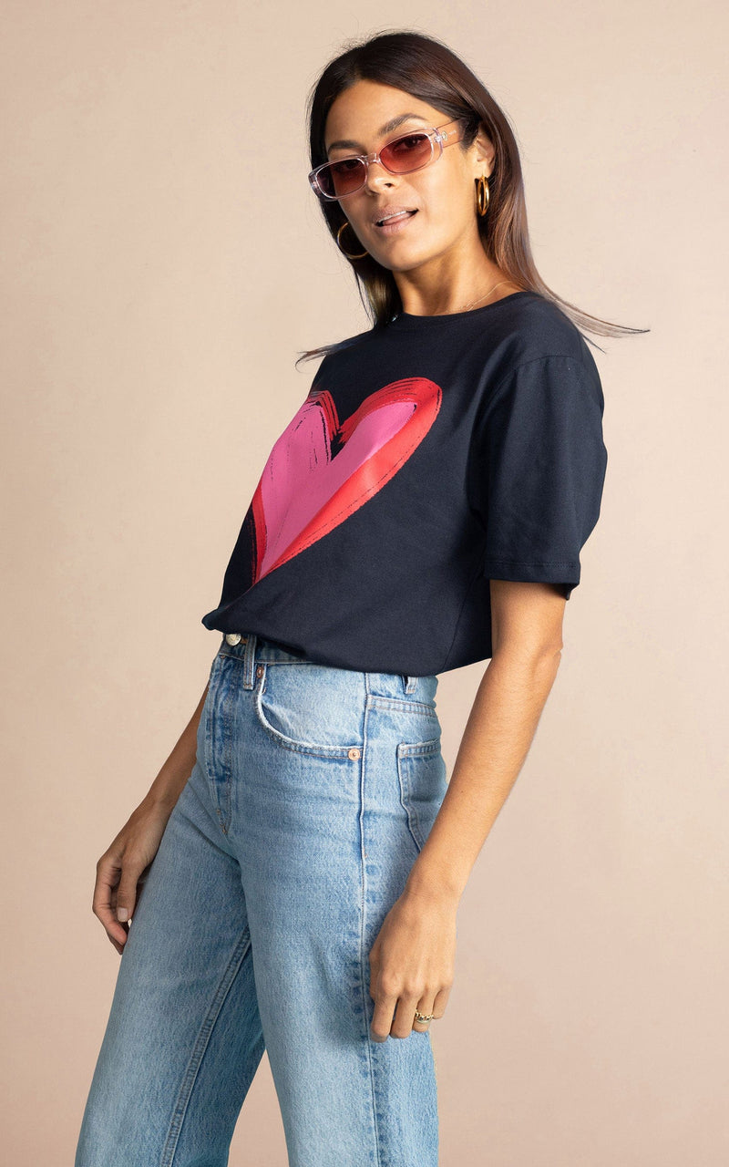 Dancing Leopard model standing sideways with sunglasses on wearing navy blue heart charity t-shirt for Choose Love tucked into light wash denim jeans