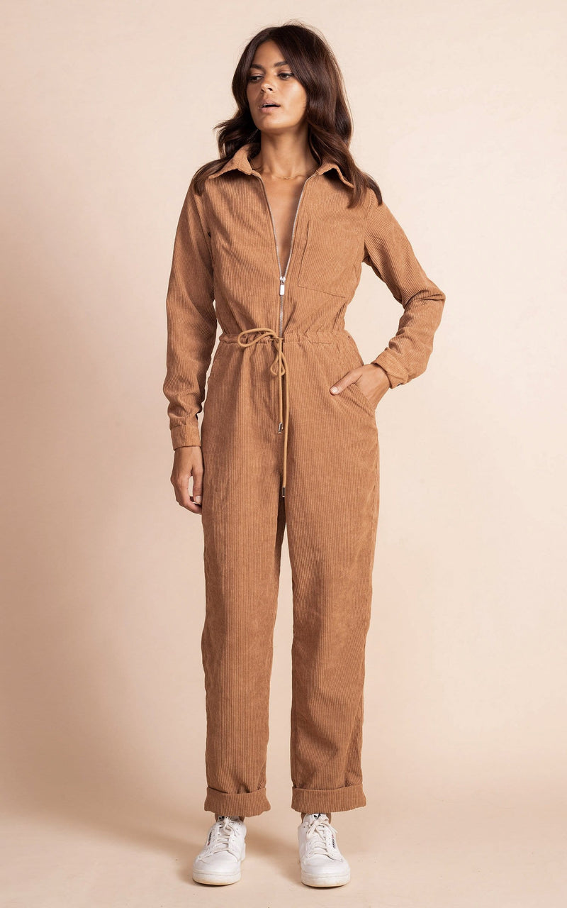 Dancing leopard model standing facing the camera with hand in pocket with tan coloured corduroy jumpsuit with white trainers