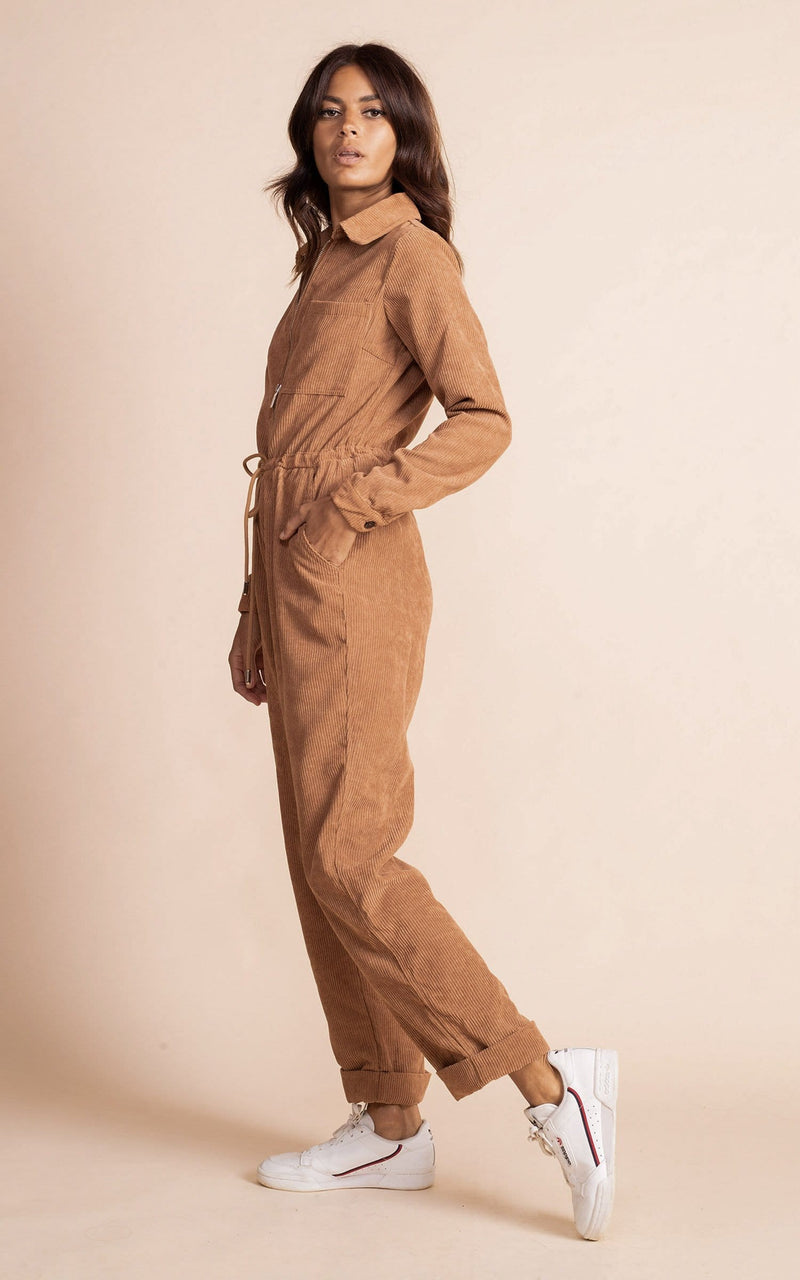 Dancing leopard model standing side to the camera with hand in pocket with tan coloured corduroy jumpsuit with white trainers