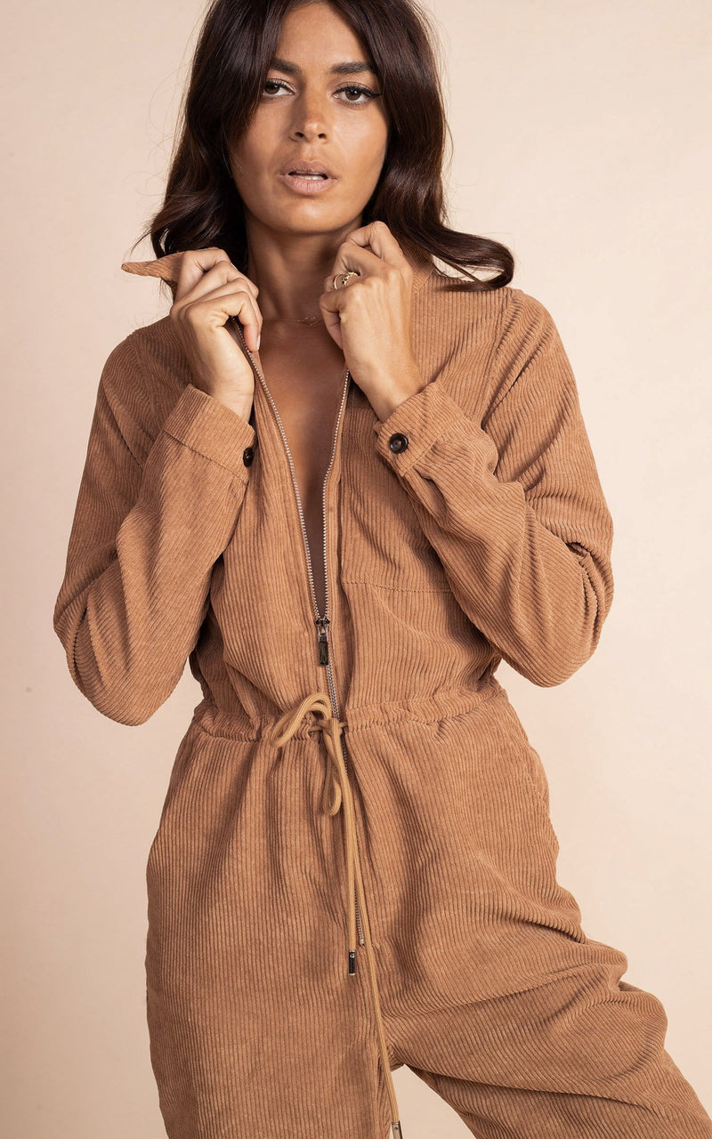 Dancing leopard model standing facing the camera with hands on collar  with tan coloured corduroy jumpsuit with white trainers