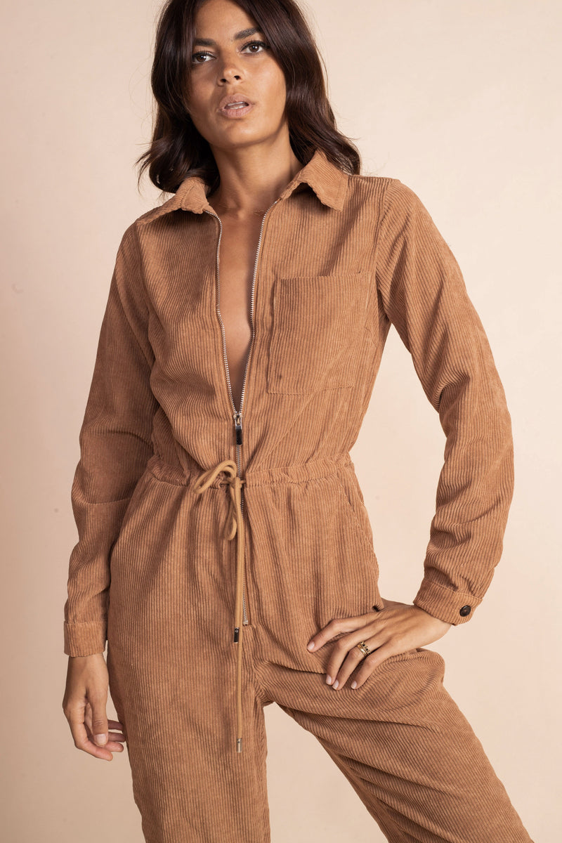 Dancing leopard model standing facing the camera with hand in leg with tan coloured corduroy jumpsuit