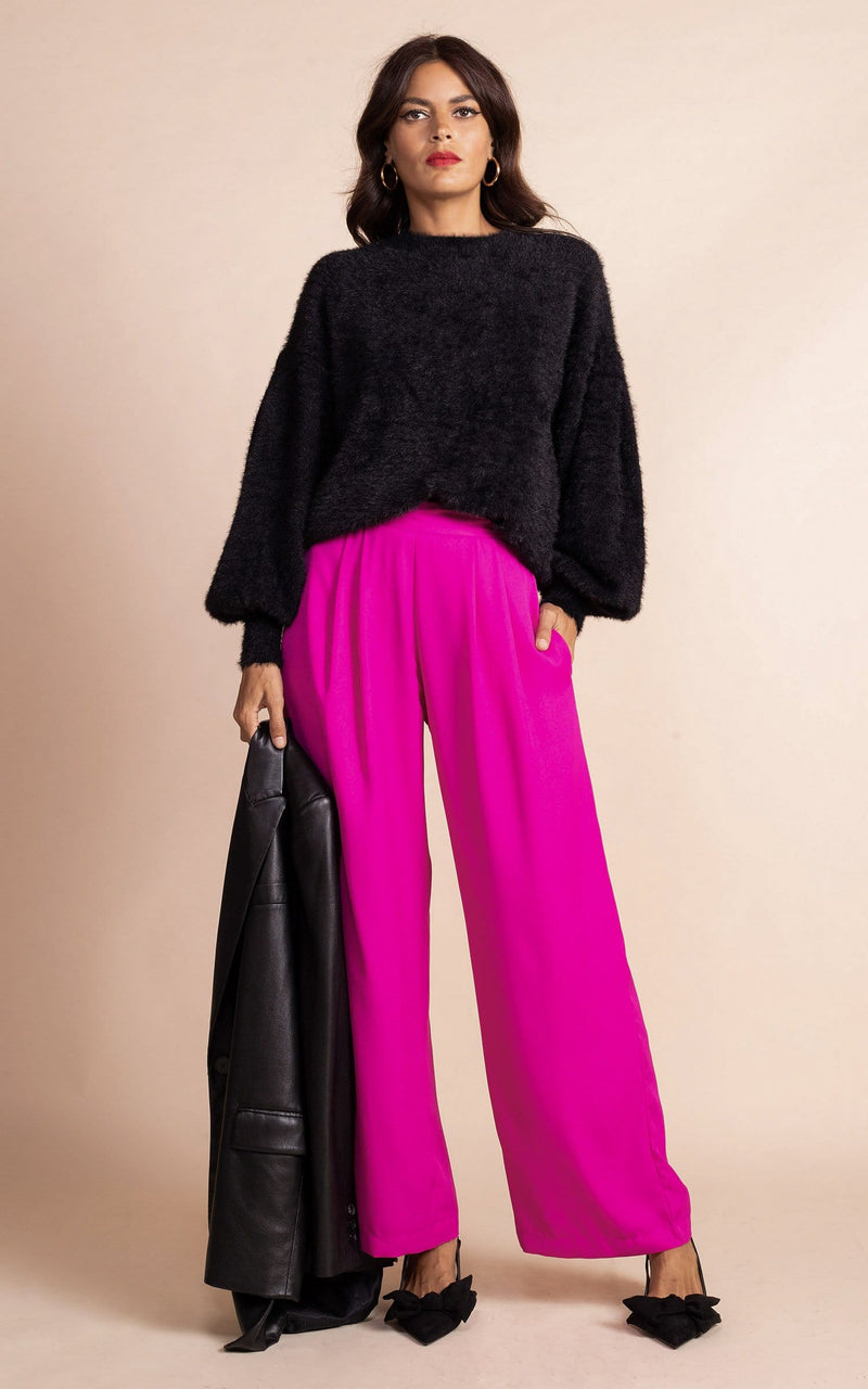 Dancing Leopard model facing the camera  wearing magenta wide leg trousers and flurry black jumper, holding a black leather blazer jacket and black pumps
