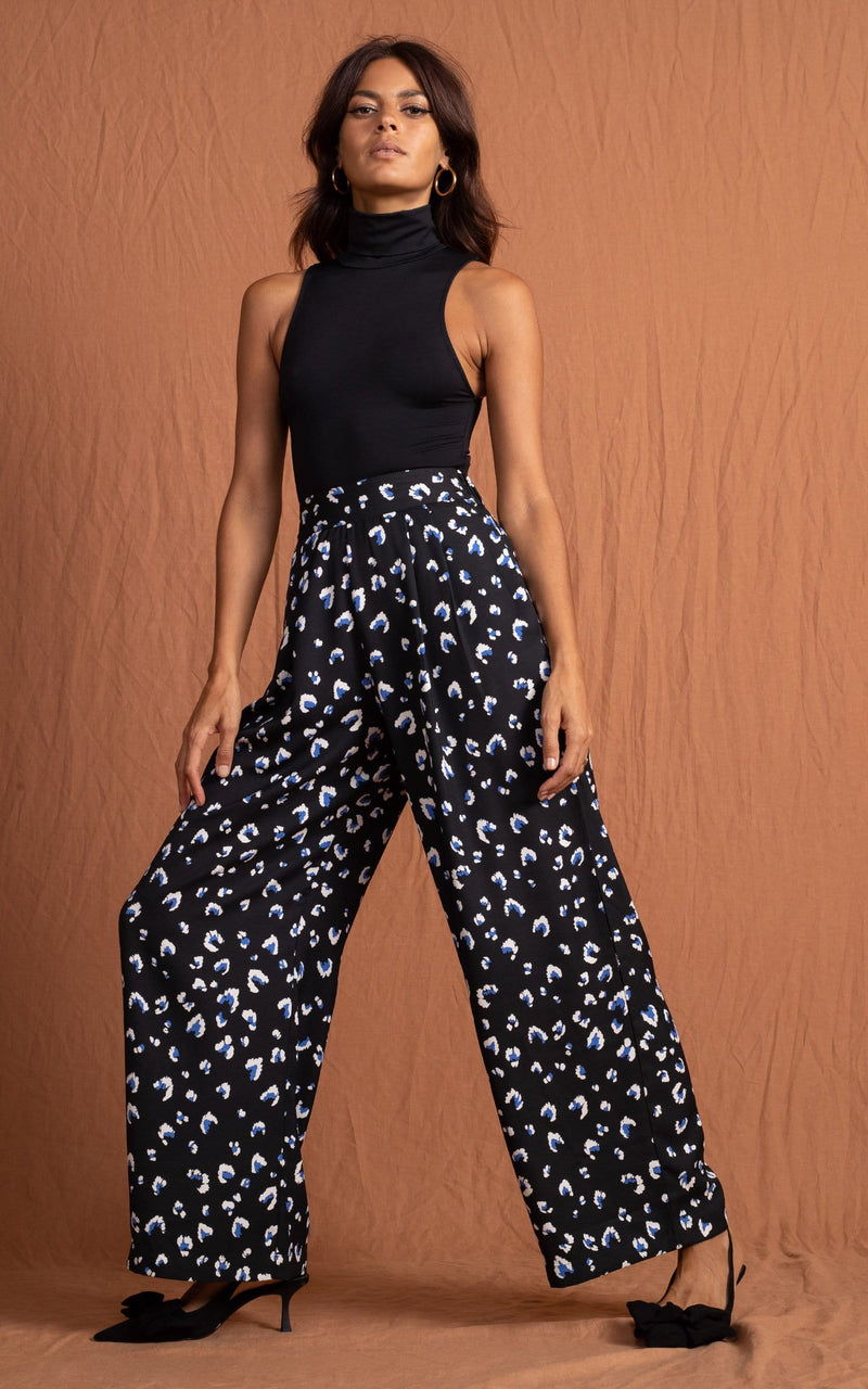 Dancing Leopard model standing front to the camera wearing a black top and wide leg black, white and navy blue leopard print trousers with black pumps