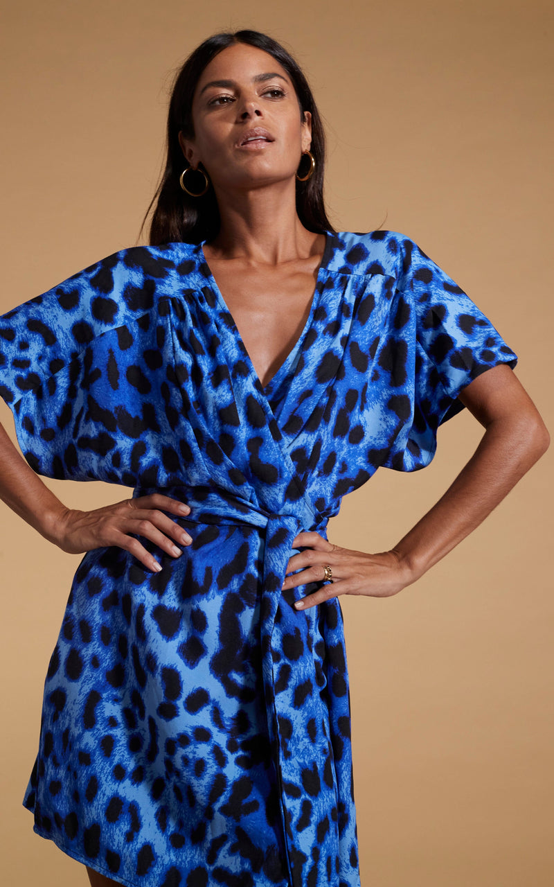 close up of Dancing Leopard model wearing Kansas Mini Wrap Dress in Bright Blue Leopard posed with hands on hips