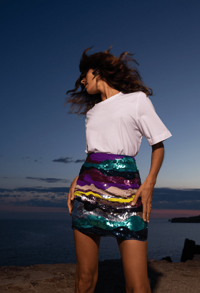 Dancing Leopard model wearing Zinnea Sequin Mini Skirt in Rainbow throwing her hair in front of sunset at beach