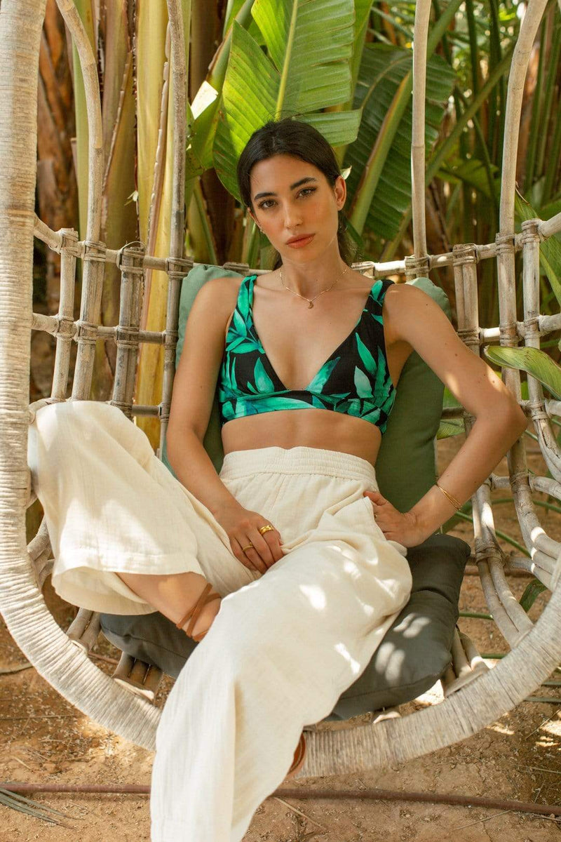 Dancing Leopard model sits on wicker chair wearing Tahiti Trousers with bikini top in tropical print 