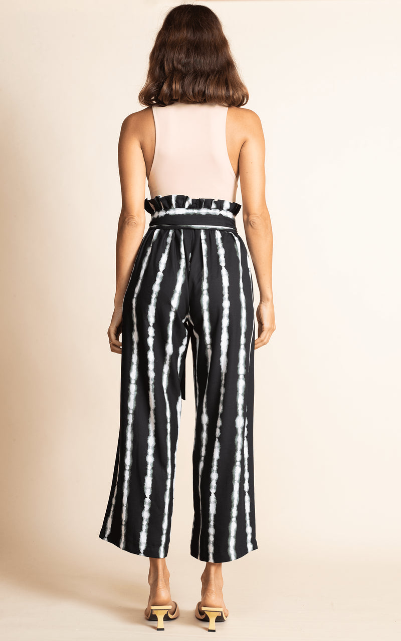 Dancing Leopard standing with back to the camera  with hand in pockets wearing black and white stripe winnie wide leg trousers with nude bodysuitt and sandals