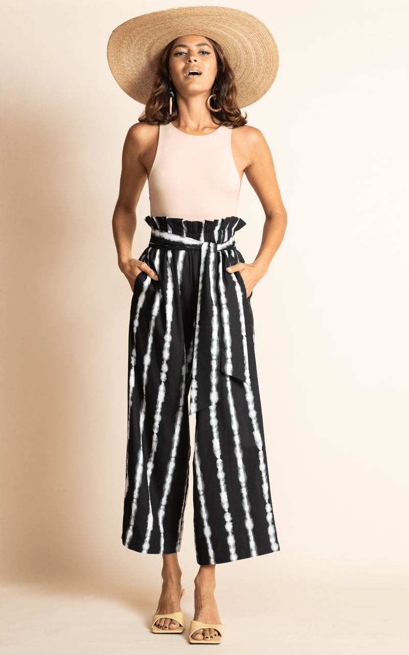 Dancing Leopard standing with hand in pockets wearing black and white stripe winnie wide leg trousers with nude bodysuit and straw hat and sandals